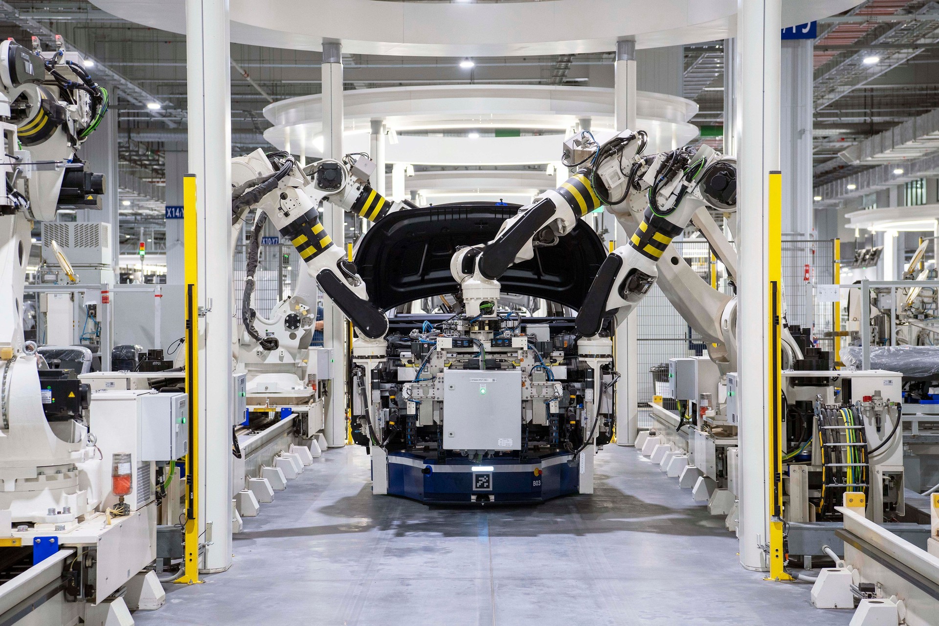 Robots handling a car body on an assembly line — before its dash, floor and trunk felt goes in